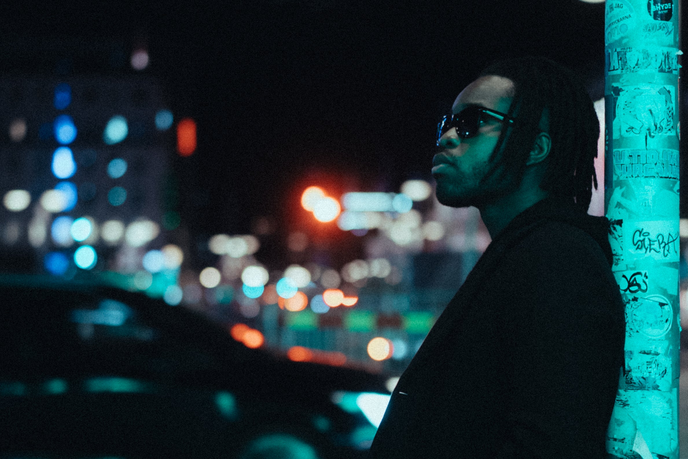 Konstnär Victor Ajayi står lutande mot en stolpe i en lugn stockholmsnatt